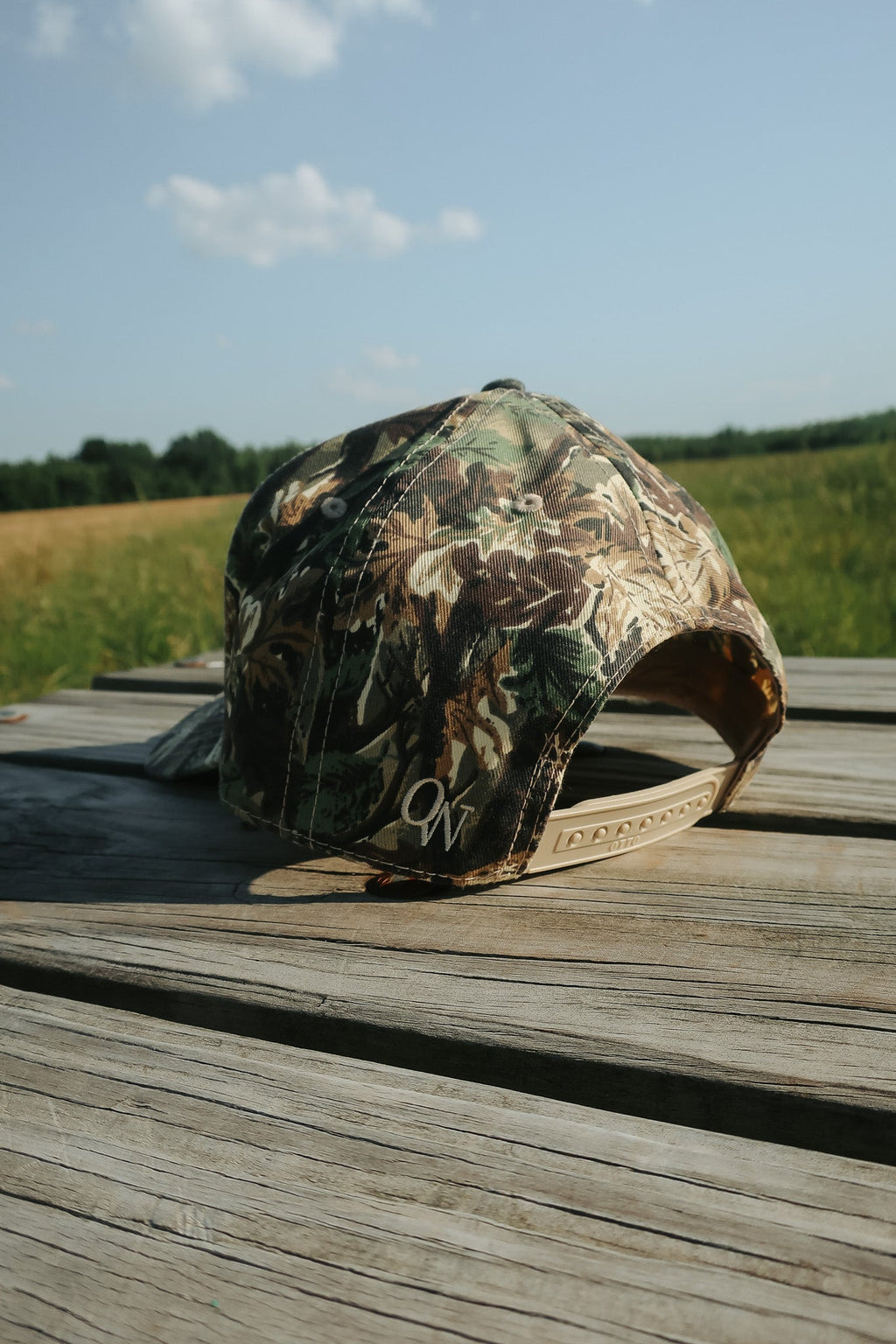 Camouflage baseball cap on a wooden surface with a field and sky in the background