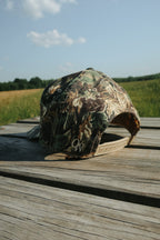 Camouflage baseball cap on a wooden surface with a field and sky in the background