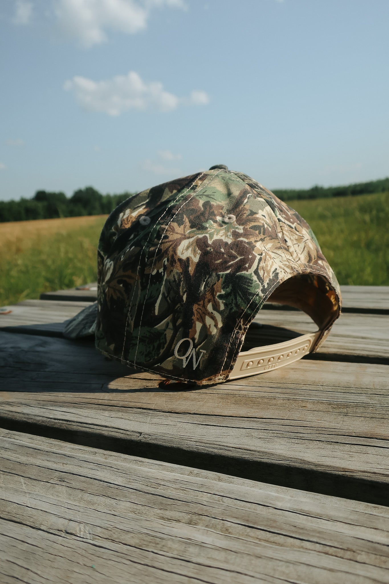 Camouflage baseball cap on a wooden surface with a field and sky in the background